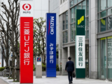 Corporate signs for Japan's leading financial institutions, MUFG, SMBC, and Mizuho, standing outside a modern banking headquarters.
